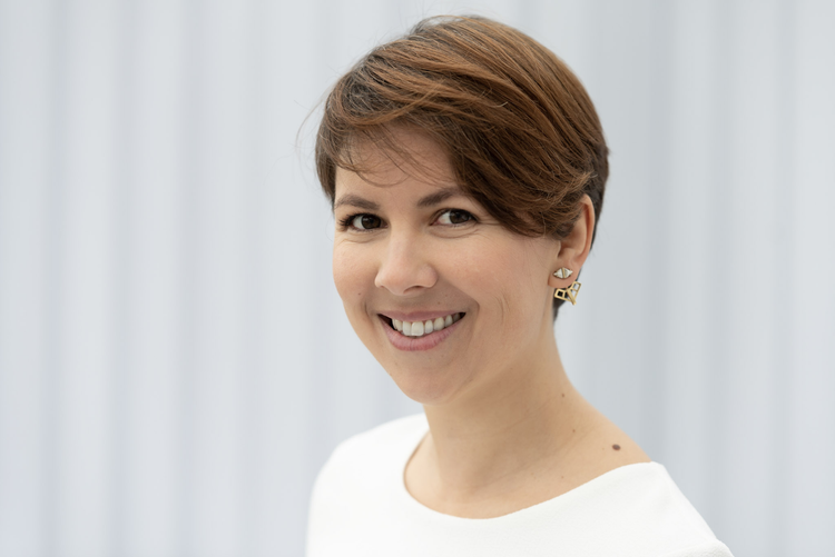 Portrait of a smiling woman with short brown hair wearing a white shirt, isolated against a blurred background. Concept for a business headshot.