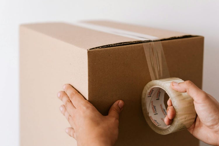 Hands sealing a cardboard box with tape, preparing it for moving out.