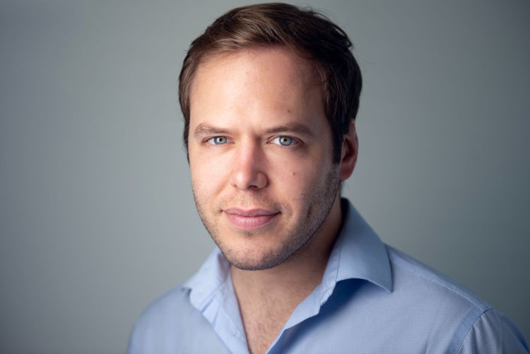 Headshot of a tech company executive, a Caucasian man in his late thirties with short brown hair and blue eyes, wearing a light-colored business casual shirt on a gray background.